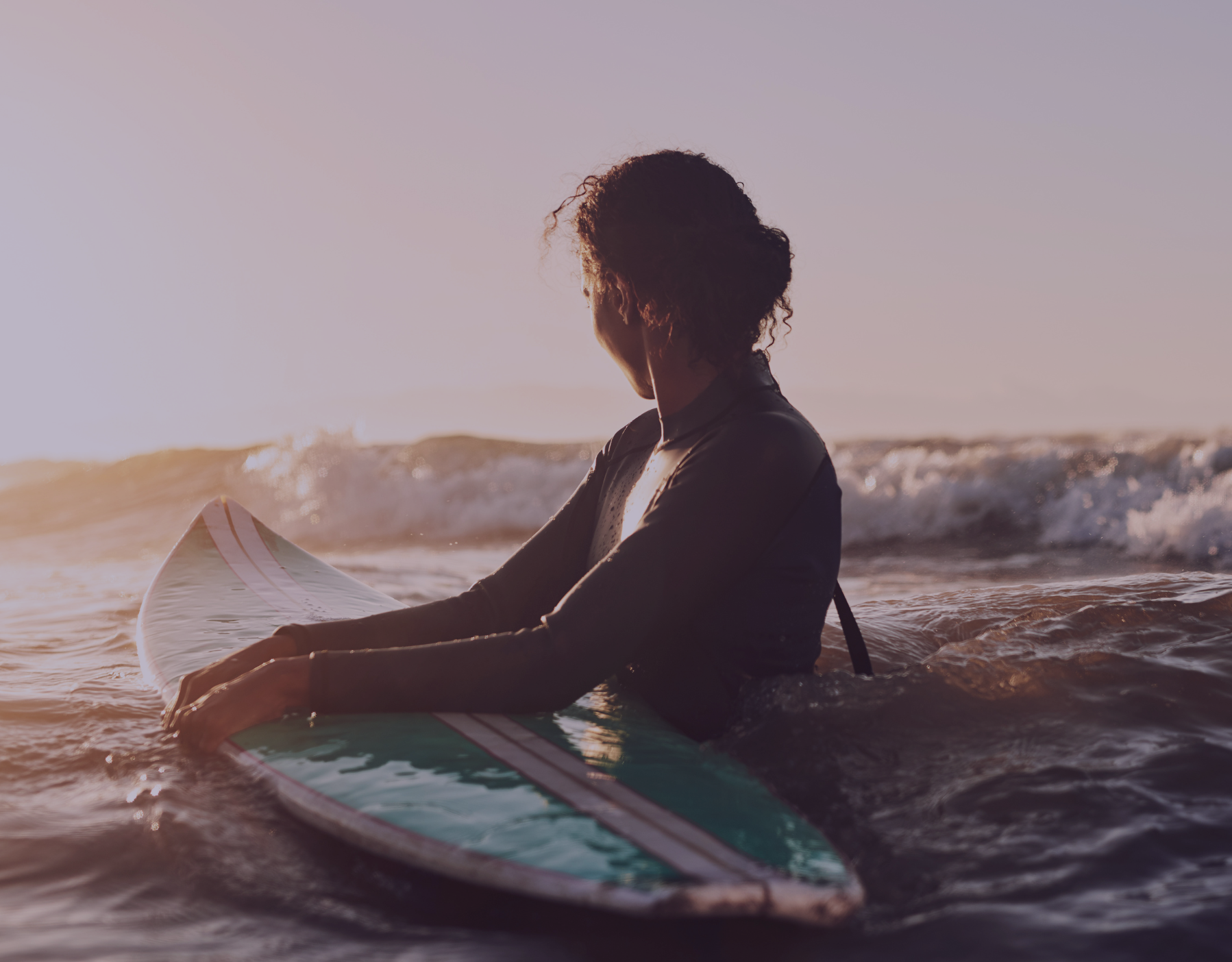 Young woman with surfboard in ocean at sunrise